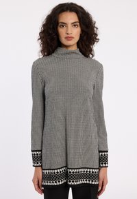 Zwart-wit gestippelde tuniek met lange mouwen en een hoge hals, voorzien van een houndstooth ontwerp en accenttrim bij de mouwen en de zoom.