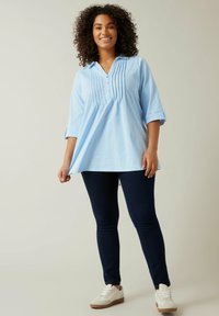 Ljusblå tunika med krag- och rundad halsringning, framfållningar och trekvartslånga ärmar, matchad med navybyxor och vita sneakers.