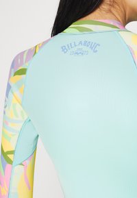 Maglietta a maniche lunghe in azzurro chiaro, con motivi colorati di foglie sulle maniche e un piccolo logo sul retro del collo. Tessuto morbido ed elasticizzato.