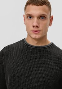 Schwarzer strukturierter Strickpullover mit Rundhalsausschnitt und grauem Saum, der ein dezentes Muster aufweist. Weicher Stoff mit lässigem Schnitt.