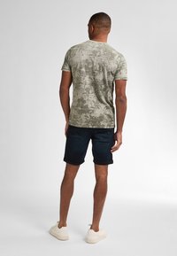 Vihreä kuviollinen t-paita lyhyillä hihoilla, yhdistettynä tummiin farkkushortseihin ja vaaleisiin tennareihin, luoden rentoa kesäasua.