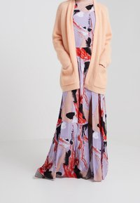 Pink knitted cardigan with pockets layered over a multicolored, flowy maxi dress featuring abstract patterns in purple, red, and black.