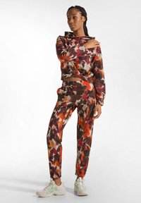 Twee-delige lounge set bestaande uit een cropped hoodie en tapered broek. De stof heeft een kleurrijk abstract patroon in rood, bruin en beige.
