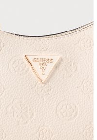 Witte synthetische handtas met reliëfpatroon en gouden driehoekig logo met de tekst "GUESS USA." Ritsdetail aan de rand.