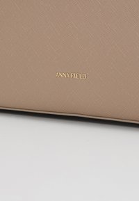 Beige texturovaná taška s jemným geometrickým vzorem, s logem "ANNA FIELD" ve zlaté barvě. Hladký materiál se strukturovaným tvarem.
