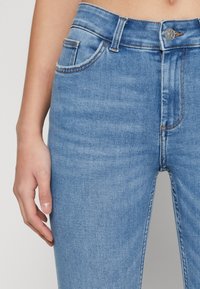 Light blue denim jeans with a smooth texture, featuring a button closure, pockets, and stitched accents along the seams.