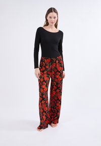 Top negro de manga larga combinado con pantalones negros fluidos que presentan un estampado floral rojo y una cinturilla elástica con cordón.