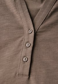 Detailní záběr na béžový pletený oděv se třemi malými kulatými knoflíky na přišité léze.