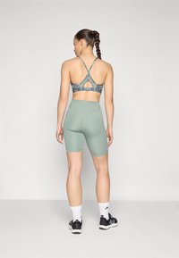 Grønn sports-BH med kryssede stropper og utskåret rygg, kombinert med høytlivs mintgrønne sykkelshortser. Teksturert stoff, elegant design.