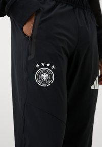 Schwarze Sporthosen mit einer Reißverschlusstasche, Logo des Deutschen Fußballbundes mit fünf Sternen und Adidas-Streifen. Glatte Textur.