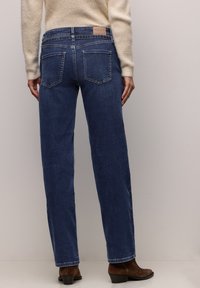 Tmavě modré džíny se rovnými nohavicemi, vysokým pasem, pětipoklopovým designem a koženou nášivkou na zadní straně. Mají viditelné švy.