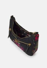 Černá prošívaná kabelka s růžovými a žlutými květinovými vzory, zlatými zipy a otevřeným vrchem, který odhaluje květinovou podšívku s kapsou na zip.