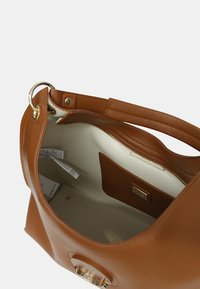 Bruine leren tas met een gladde textuur, ruime binnenkant, crèmekleurige voering en een ritsvak. Voorzien van ronde hardware aan de voorkant.