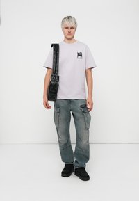 Lys lilla kortærmet t-shirt med sort grafisk tryk, parret med løse grå cargo bukser. Accessories inkluderer en sort crossbody taske og sorte sko.