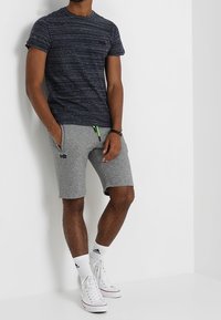 Námořnické textured tričko s krátkým rukávem, spárované se šedými šortkami s kapsami a šňůrkou. Bílé vysoké tenisky dodávají celkovému outfitu konečnou podobu.