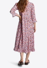 Robe maxi à imprimé floral en rose, violet et blanc avec des manches cloche de 3/4 et un ourlet volanté. Portée avec des sandales à talons carrés brunes.