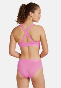 Vaaleanpunainen urheiluliivimalli, jossa on ristikkäiset hihnat, sekä siihen sopivat hipster-pikkarit. Pehmeä kangas; logo kummankin vaatteen vyötäröllä.