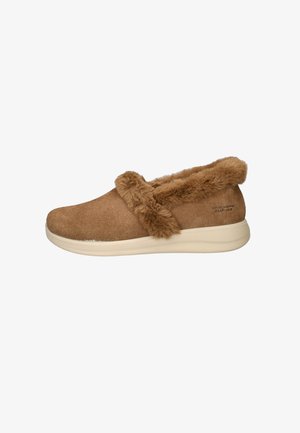 Bruine suède instap schoen met fluffy nep-bont rand, witte rubberen zool en het logo "SKECHERS SLIP-INS" nabij de hak.