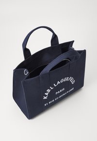 Navy blue canvas tote bag with double handles, featuring white text and a zipper. Rectangular shape, sturdy design.
