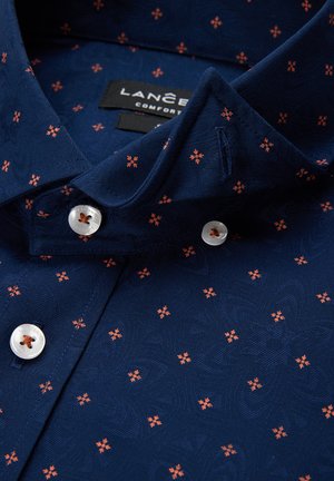 Granatowa koszula z teksturowanym wzorem małych pomarańczowych kwiatów, spiczasty kołnierzyk oraz białe guziki z centralnym otworem.