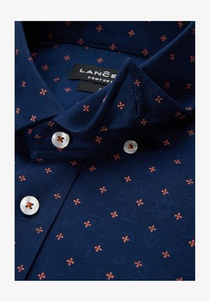 Granatowa koszula z teksturowanym wzorem małych pomarańczowych kwiatów, spiczasty kołnierzyk oraz białe guziki z centralnym otworem.