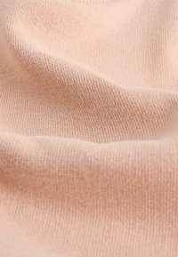 Tissu tricoté rose pâle doux avec une texture fine, montrant de doux plis et une surface lisse.