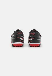 Botas de fútbol negras con acentos rojos, con un diseño texturizado, forma de perfil bajo y una suela de goma con tacos pronunciados para proporcionar agarre.