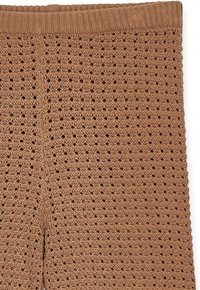 Rjave pletene hlače z nasičenim dizajnom, ki vsebuje odprte zanke in širok žametni pas. Tkanina se zdi lahka in zračna.