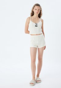 Conjunto de loungewear de color crema, tejido, que incluye un top corto con un gráfico de cereza y pantalones cortos a juego, combinado con zapatillas grises de felpa.