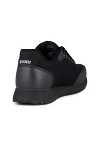 Baskets de sport noires avec des détails en mesh et cuir, talon texturé, fermeture à lacets et logo "WODEN" à l'arrière.