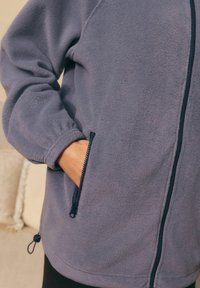 Fleece jack in gedempt grijs met een rits aan de voorkant, elastische manchetten, zijzakken met ritsen en verstelbare hem toggles voor een goede pasvorm.