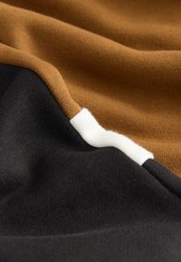 Tissu de pull avec des couleurs marron, noir et blanc. Texture douce avec un motif tricoté visible, mettant en valeur les sections de couleurs contrastées.