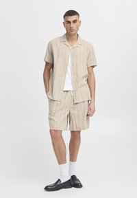 Beige, short-sleeve shirt with vertical stripes, paired with matching shorts. Black loafers and white socks complete the outfit.