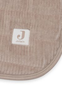 Tapis de sol rond beige avec une texture striée, surface douce et bords cousus. Présente une petite étiquette avec le nom de la marque "Jollein."