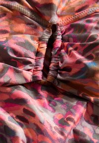 Kleurrijke, gestreepte stof met tinten roze, oranje en grijs. Gevarieerd, ribbelachtig materiaal met een geplooid ontwerpdetail.