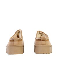 Chaussures slip-on en daim beige avec une tige douce en suède, une couture blanche contrastante autour du col, et une semelle plateforme modérée avec un dessous texturé.
