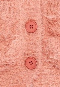 Två runda korallknappar sydda på mjuk, ludden rosa stickad tyg, som framhäver textur och kläddetaljer.