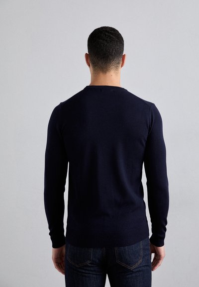 Marineblaues Strickpullover mit langen Ärmeln und einem runden Ausschnitt, ausgestattet mit gerippten Bündchen und Saum. Kombiniert mit dunklen Denim-Jeans, die eine glatte Textur zeigen.