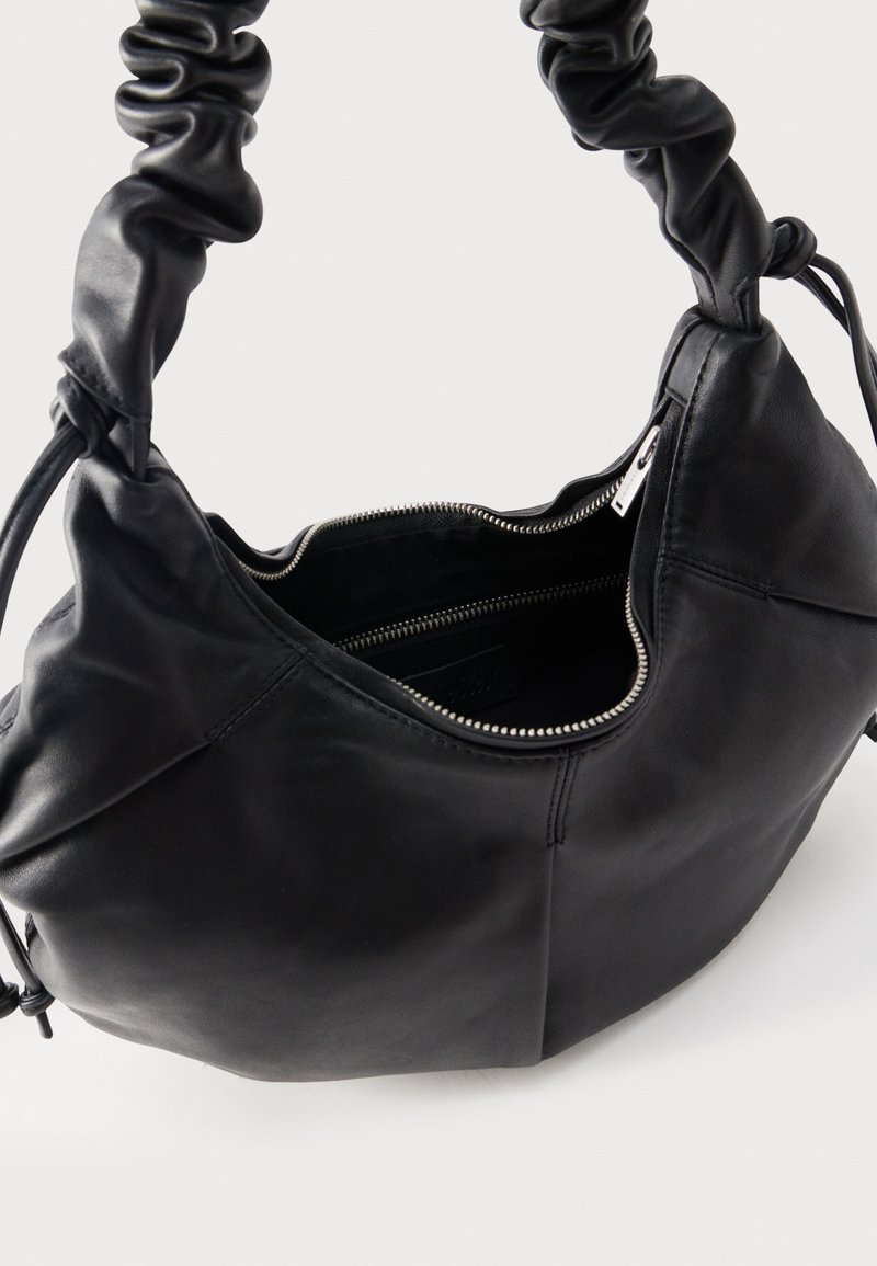 Sac à main en cuir noir avec poignée froncée, fermeture éclair ouverte révélant une poche intérieure et surface extérieure lisse.