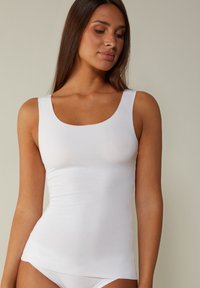 Hvid tanktop med en bred udringet hals, lavet af glat, strækbart stof. Den har en tætsiddende silhuet uden synlige mønstre eller detaljer.