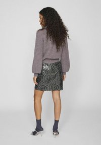 Suéter morado texturizado con mangas abullonadas, combinado con una mini falda negra de lentejuelas con un patrón en espiral, llevada con calcetines de canalé en azul marino y sandalias.