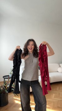 Topuri fără mâneci, de culoare neagră și roșie, cu accente de volane, realizate dintr-un material ușor, ținute de o persoană într-un mediu casual.