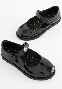 Zapatos de charol negro tipo Mary Jane con punta redonda, correa ajustable y plantilla texturizada con patrón de estrellas. Suela plana y resistente en color negro.