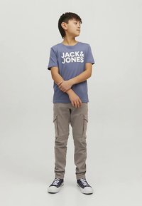 Μπλε βαμβακερό μπλουζάκι με το λογότυπο "JACK & JONES" σε λευκά γράμματα, συνδυασμένο με ανοιχτό μπεζ cargo παντελόνι και μπλε αθλητικά με λευκές σόλες.