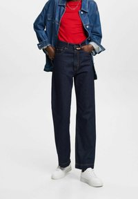 Dark denim wide-leg jeans with front pockets, contrasting orange stitching, and a high waist. Paired with a red t-shirt and denim jacket.