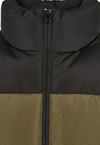 Puffjacka med hög krage, dragkedjestängning, svart överdel och olivgrön underdel med en slät, quiltad textur.