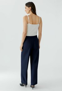 White tank top with thin straps, paired with wide navy trousers and black heels, showcasing a smooth fabric texture and tailored fit.