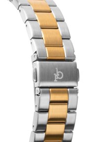 Kaksitooniline metallkellarihm, mis koosneb vahelduvatest harjatud hõbedast ja kuldsetest roostevabast terasest linkidest, millel on ristkülikukujuline kinniti ja reljeefne logo detail.