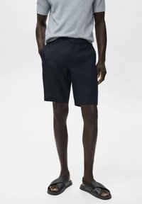 Pantaloni corti blu navy realizzati in tessuto texturizzato, con una linea dritta e tasche laterali, abbinati a sandali neri con fascia.