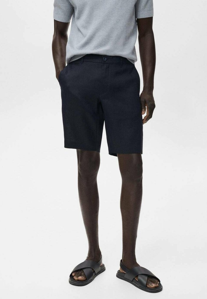 Pantaloni corti blu navy realizzati in tessuto texturizzato, con una linea dritta e tasche laterali, abbinati a sandali neri con fascia.